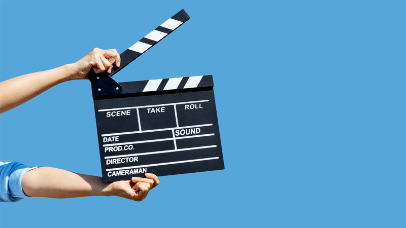 A man in a blue shirt holds a movie clapperboard
